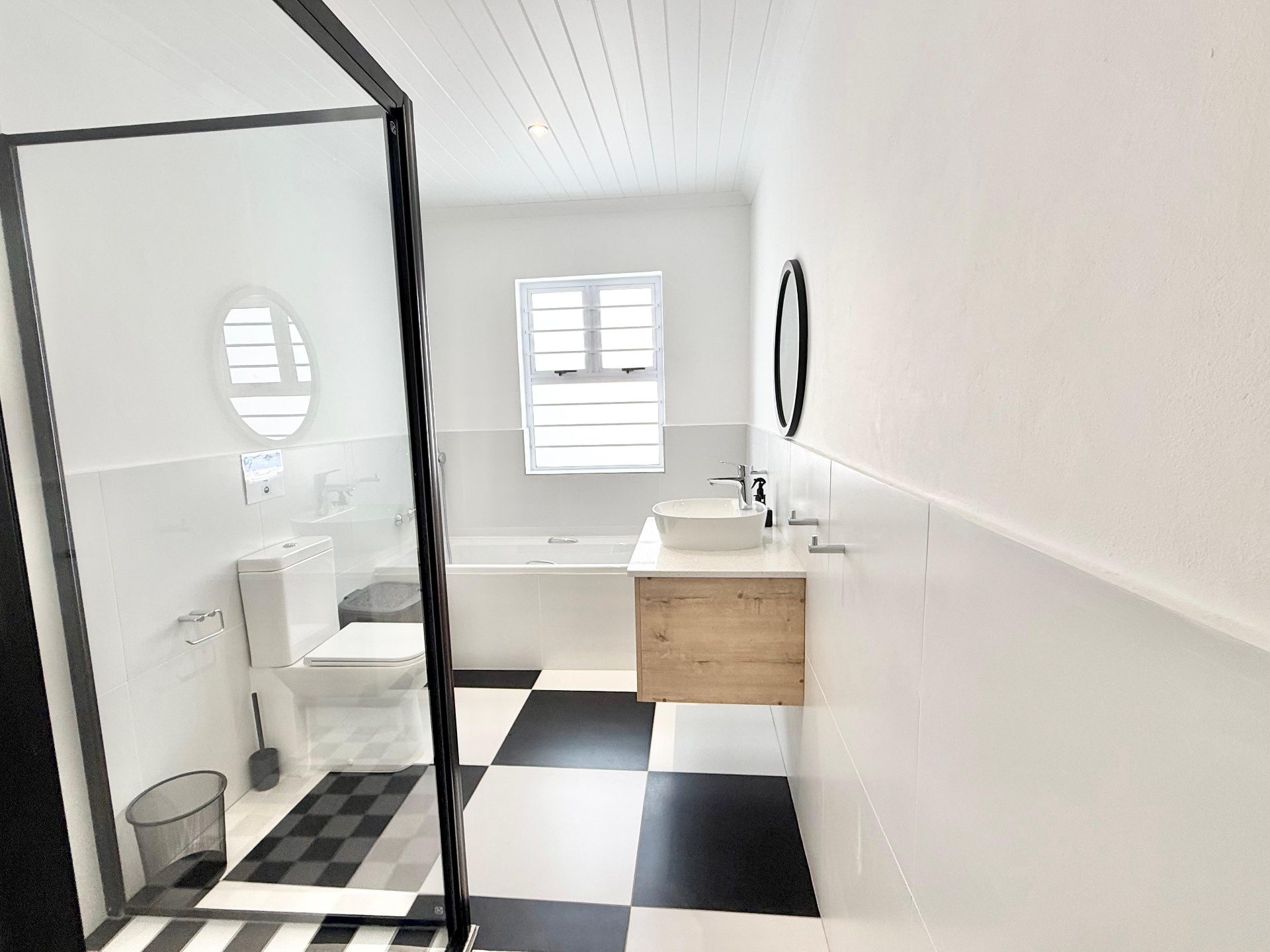 Bathroom with tub, checkerboard floor and round mirror